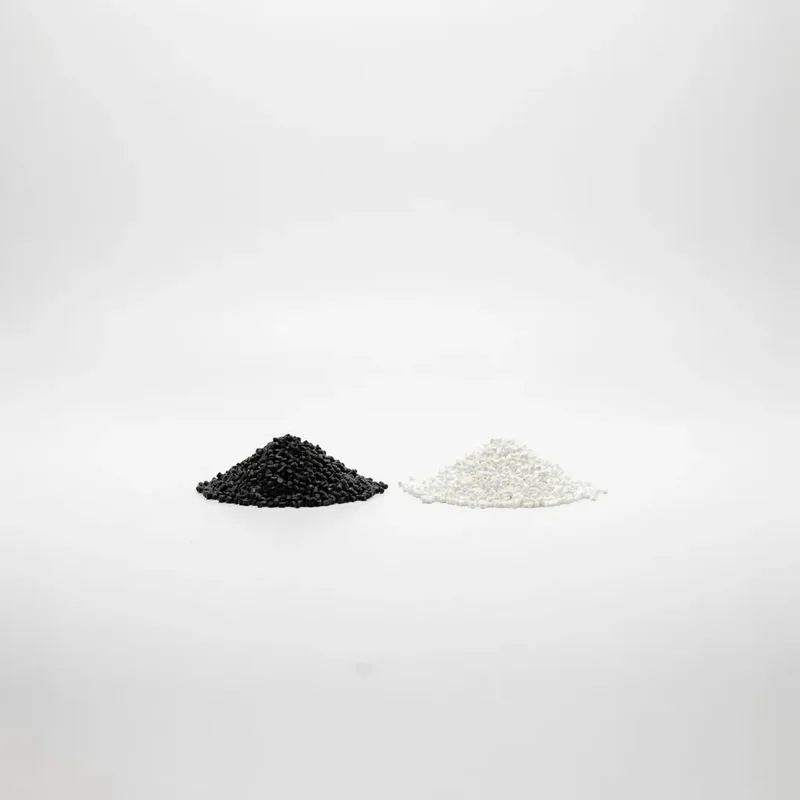 Pequeños pellets de masterbatch negro y blanco lado a lado sobre un fondo blanco limpio