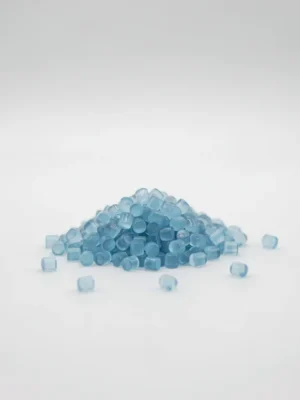 Pequeños gránulos de masterbatch CAM-3012 translúcidos azul claro sobre un fondo blanco limpio